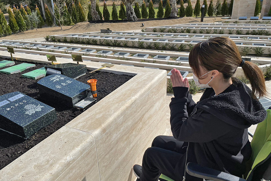 お墓の前で手を合わせる車椅子の女性