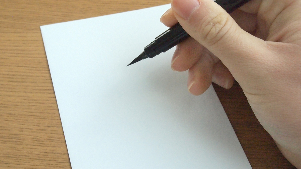白い無地の封筒に筆ペンで文字を書こうとしている