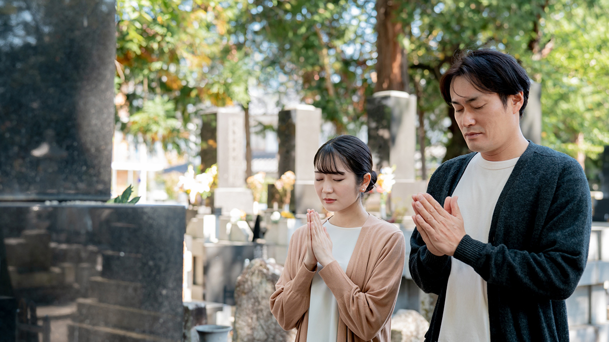 お墓に手を合わせている男女