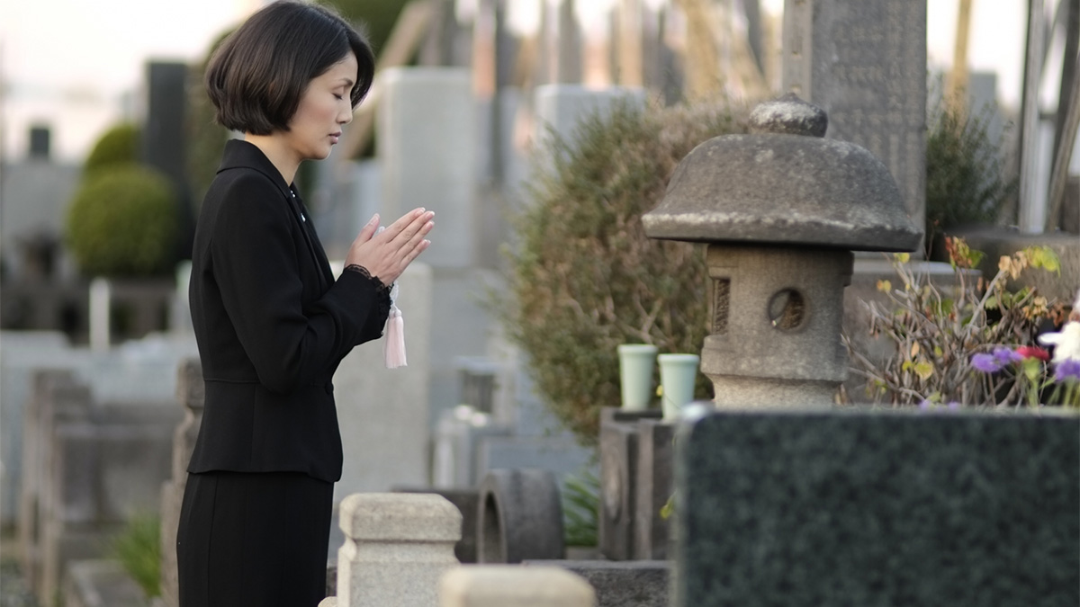 お墓の前で手を合わせる女性